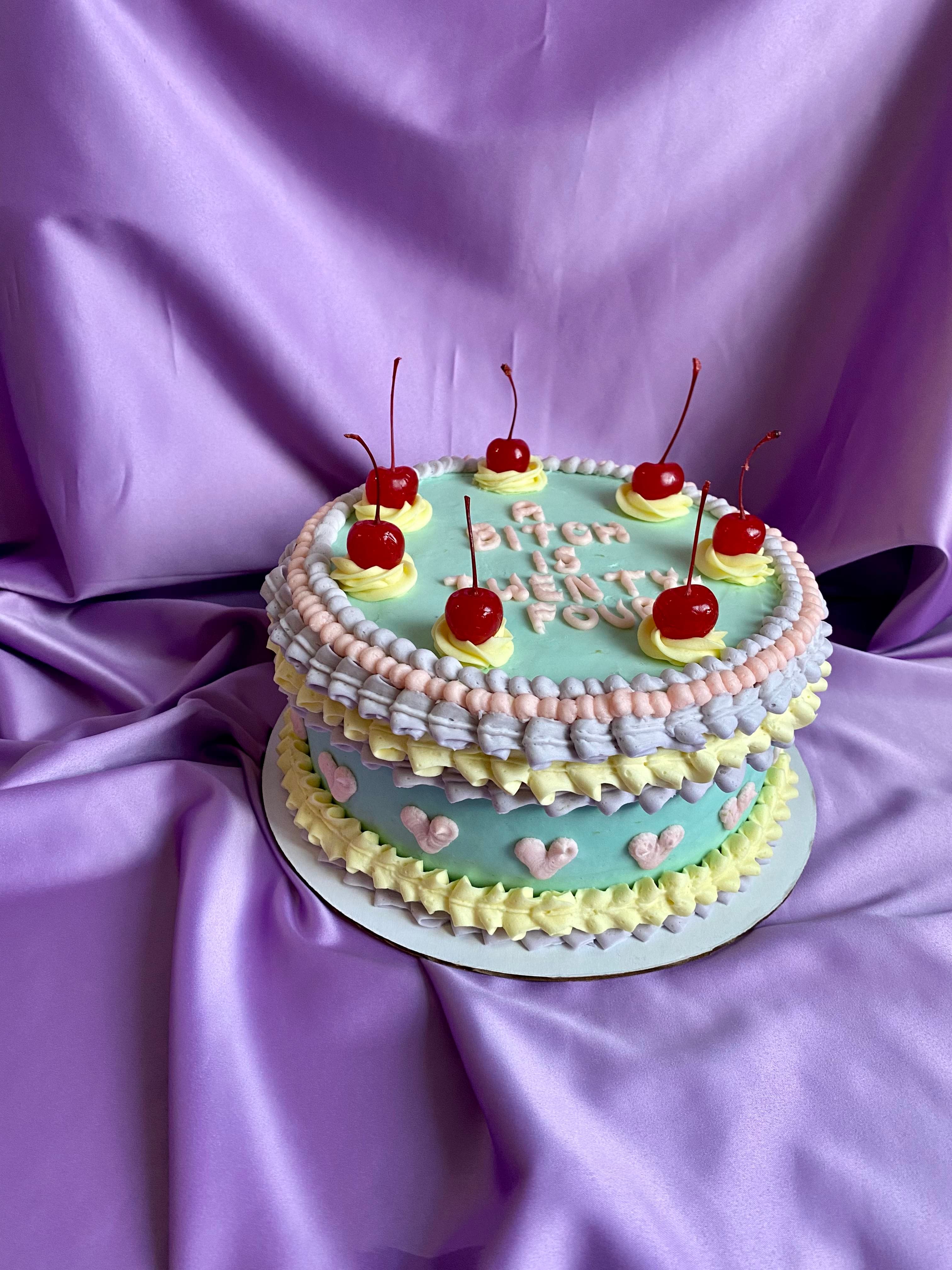 photo of a round cake in pastel colors with frills and cherries on top