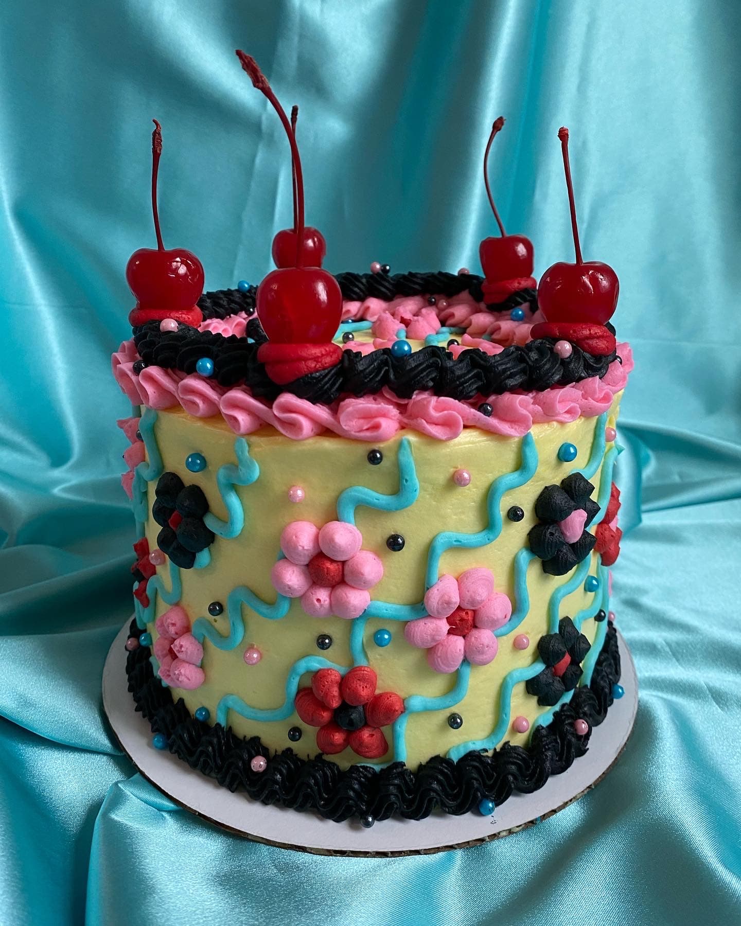 photo of a round cake with piped daises and cherries on top