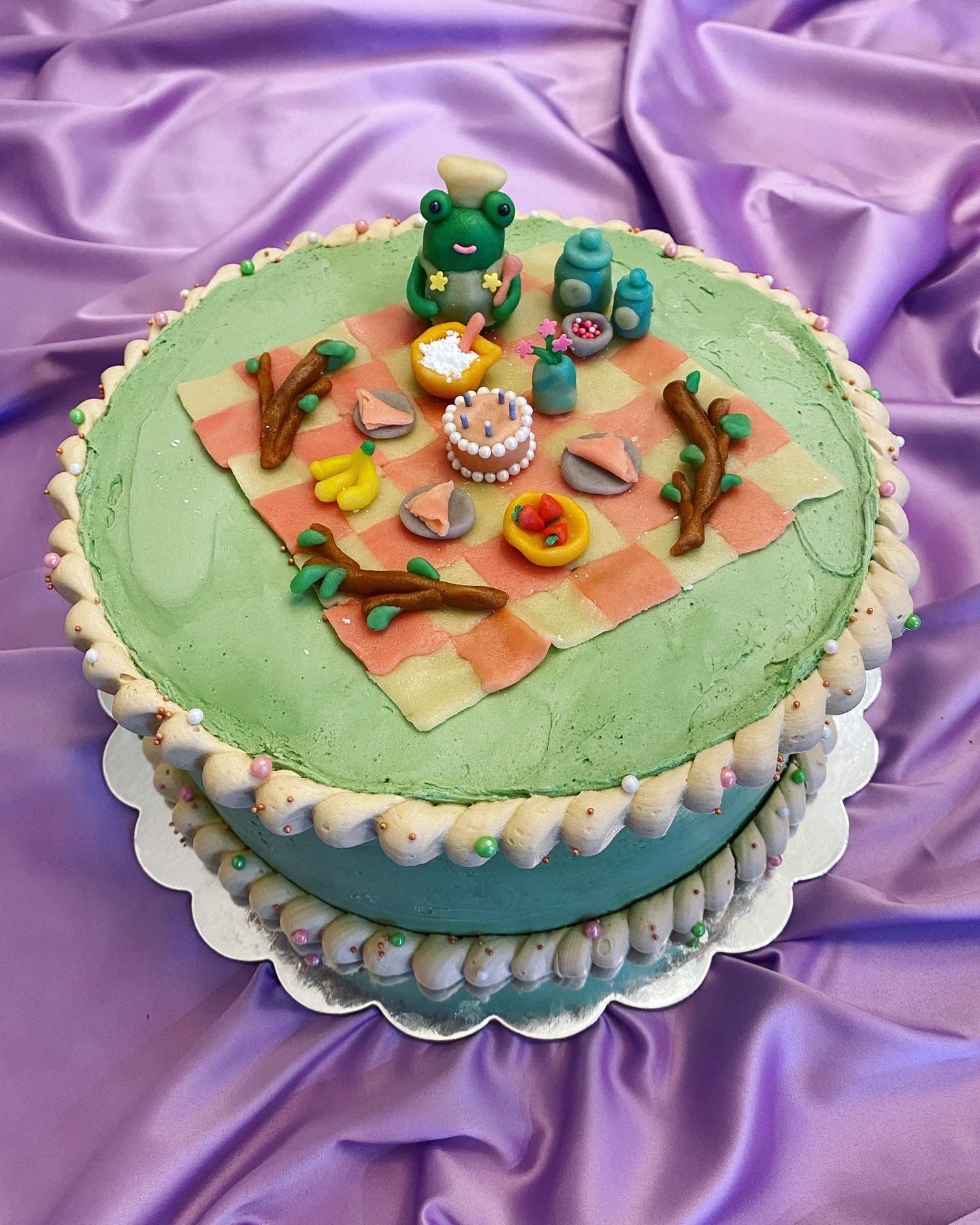 photo of a round cake with a marzipan sculpted frog making a cake and preparing for a party