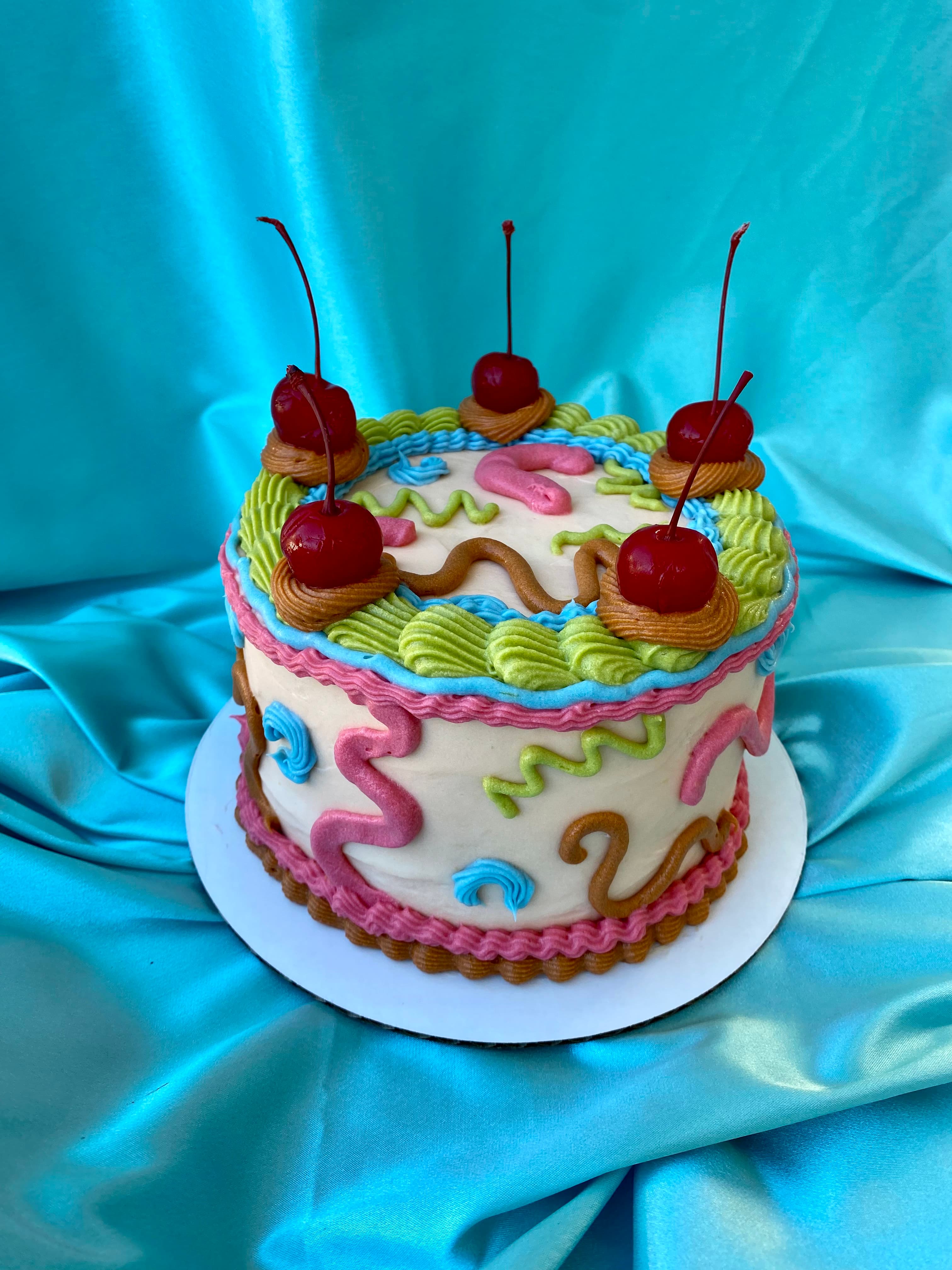 photo of a round cake with squiggles and cherries on top