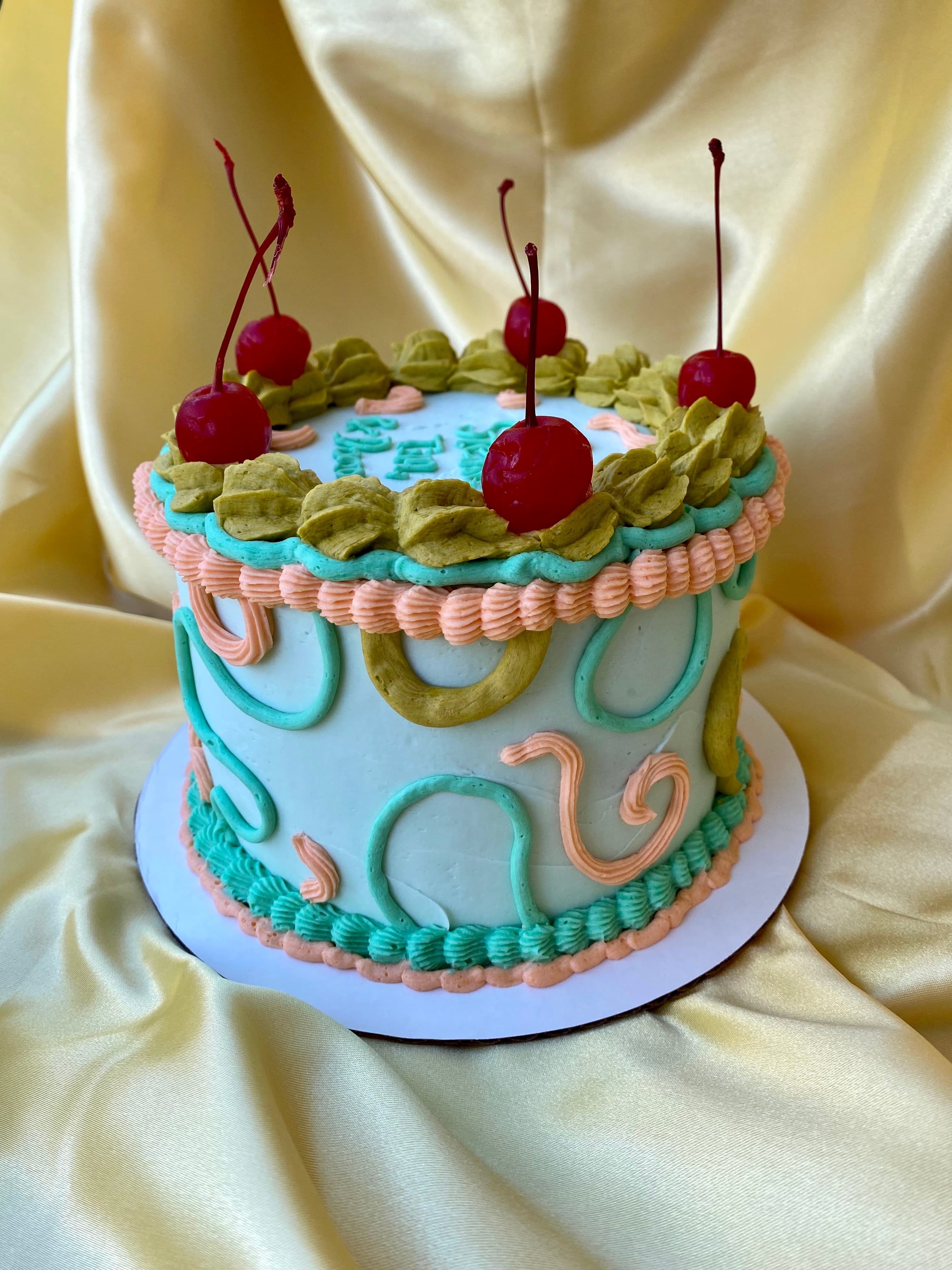 photo of a round cake with squiggles and cherries on top